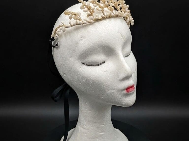 Tiara de novia antigua de cera y azahar sobre maniquí con fondo negro, época victoriana circa 1900.